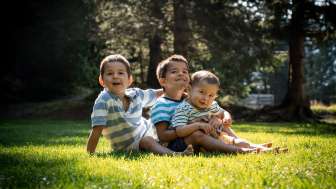 Tre bambini sono seduti su un prato soleggiato ai margini del bosco.